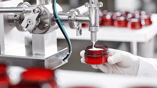 Red jar being filled with cosmetic cream